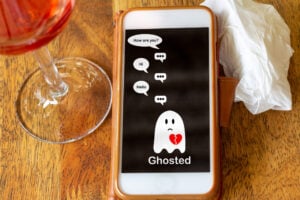 Ghosted on mobile phone on table with glass of wine and tissue, Ghosting to cut all communication without explanation, ending a relationship. Social media dating.