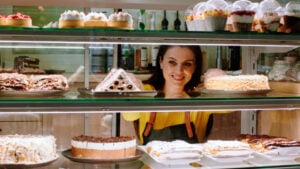 A woman looking at shelves of cakes in a bakery while smiling.