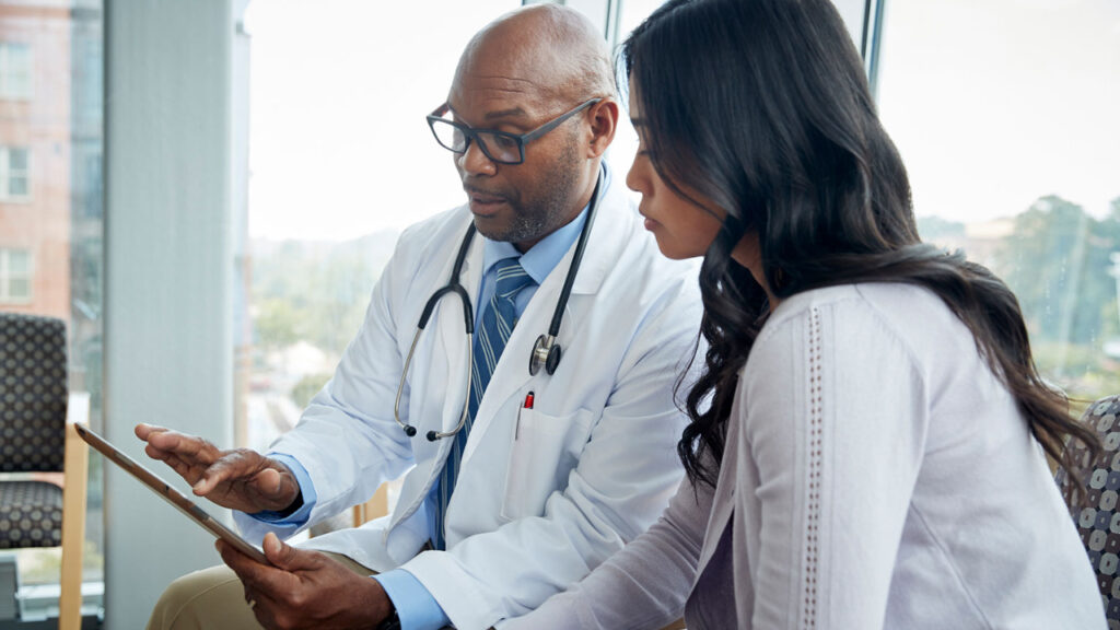 a male doctor talking to a female patient while looking at a digital tablet