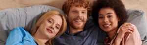 Three people lay in a bed smiling